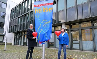 Bürgermeisterin Susanne Rutenkröger (links) und Gleichstellungsbeauftragte Dorit Bethke hissen die Fahne „Nein zu Gewalt an Frauen!“ auf dem Rathausplatz. - Stadt Bünde Bürgermeisterin Susanne Rutenkröger (links) und Gleichstellungsbeauftragte Dorit Bethke hissen die Fahne „Nein zu Gewalt an Frauen!“ auf dem Rathausplatz. - Stadt Bünde
