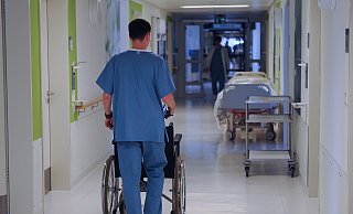 Ein Pfleger schiebt mit einen Rollstuhl über einen Flur. - picture alliance / dpa Ein Pfleger schiebt mit einen Rollstuhl über einen Flur. - picture alliance / dpa