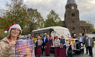 Karin Heimke zeigt das Plakat für den Rehmer Weihnachtsmarkt. Im Hintergrund sind ihre Mitorganisatoren zu sehen, der Oldtimerbus und natürlich die Rehmer Kirche. - Nicole Sielermann Karin Heimke zeigt das Plakat für den Rehmer Weihnachtsmarkt. Im Hintergrund sind ihre Mitorganisatoren zu sehen, der Oldtimerbus und natürlich die Rehmer Kirche. - Nicole Sielermann