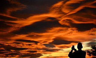 Das Naturschauspiel festhalten: Ein Mann fotografiert einen Sonnenuntergang. - Laurent Gillieron/KEYSTONE/dpa Das Naturschauspiel festhalten: Ein Mann fotografiert einen Sonnenuntergang. - Laurent Gillieron/KEYSTONE/dpa