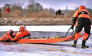 Dennis Streitbürger (rechts) hält den Schlitten, Philipp Lemmen zieht Bernd Dieske aus dem See. Er hatte sich für die Feuerwehr-Übung in den eiskalten Johannisbach gestürzt. Einige Spaziergänger schauten zu . Dennis Streitbürger (rechts) hält den Schlitten, Philipp Lemmen zieht Bernd Dieske aus dem See. Er hatte sich für die Feuerwehr-Übung in den eiskalten Johannisbach gestürzt. Einige Spaziergänger schauten zu .