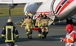 Einsatzkräfte der Feuerwehr tragen einen Verletzten, der bei der Notfallübung aus dem Flugzeug gerettet wurde, zur Sammelstelle. - Ralph Meyer Einsatzkräfte der Feuerwehr tragen einen Verletzten, der bei der Notfallübung aus dem Flugzeug gerettet wurde, zur Sammelstelle. - Ralph Meyer
