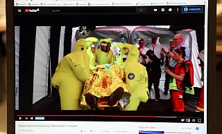 Sequenz mittendrin: Ein Filmausschnitt, der die Arbeit der Helfer unter erschwerten Bedingungen in Schutzanzügen zeigt. - Screenshot: Simone Flörke Sequenz mittendrin: Ein Filmausschnitt, der die Arbeit der Helfer unter erschwerten Bedingungen in Schutzanzügen zeigt. - Screenshot: Simone Flörke