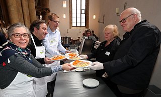 Ulrike Mann, Vincenzo Copertino, Joachim Hood (v.l.) tragen als ehrenamtliche Kellner weiße Schürzen mit Vesperkirchen-Logo und Namensschild. Wolfgang Ruwe und Anita Albers (v.r.) füllen an der Essensausgabe auf. - Wolfgang Rudolf Ulrike Mann, Vincenzo Copertino, Joachim Hood (v.l.) tragen als ehrenamtliche Kellner weiße Schürzen mit Vesperkirchen-Logo und Namensschild. Wolfgang Ruwe und Anita Albers (v.r.) füllen an der Essensausgabe auf. - Wolfgang Rudolf