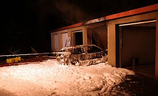 Das ausgebrannte Autowrack wurde von den Einsatzkräften mit einem Gurt aus der Garage gezogen. Der Löschschaum bedeckte großflächig den Hof. - Polizei Kreis Minden-Lübbecke Das ausgebrannte Autowrack wurde von den Einsatzkräften mit einem Gurt aus der Garage gezogen. Der Löschschaum bedeckte großflächig den Hof. - Polizei Kreis Minden-Lübbecke