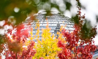 Rot-gelb-grün herbstlich verfärbte Blätter sind an Bäumen vor der Reichstagskuppel zu sehen. - Foto: Britta Pedersen/dpa-Zentralbild/dpa Rot-gelb-grün herbstlich verfärbte Blätter sind an Bäumen vor der Reichstagskuppel zu sehen. - Foto: Britta Pedersen/dpa-Zentralbild/dpa