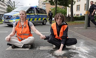 Mit einem besonders hartnäckigen Gemisch aus Klebstoff und Sand hat ein Klimakleber seine Hand auf dem Asphalt der Kreuzstraße befestigt. Ein Lösen mit Speiseöl ist unmöglich. Die andere Hand ist mit der seiner Mitstreiterin verklebt. - Paul Brinkmann Mit einem besonders hartnäckigen Gemisch aus Klebstoff und Sand hat ein Klimakleber seine Hand auf dem Asphalt der Kreuzstraße befestigt. Ein Lösen mit Speiseöl ist unmöglich. Die andere Hand ist mit der seiner Mitstreiterin verklebt. - Paul Brinkmann