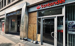 Am Tag nach dem Unfall ist die beschädigte Schaufensterscheibe der Sanstander-Filiale bereits mit Brettern gesichert. Der Eingangsbereich aus Metall ist sichtlich verbogen. - Eike J. Horstmann Am Tag nach dem Unfall ist die beschädigte Schaufensterscheibe der Sanstander-Filiale bereits mit Brettern gesichert. Der Eingangsbereich aus Metall ist sichtlich verbogen. - Eike J. Horstmann