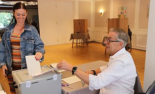 Charlene Bügler (36) hat ihr Kreuz gemacht und steckt ihren Wahlzettel unter den wachsamen Augen von Wahlhelfer Bruno Obens in die Wahlurne. - Claus Frickemeier Charlene Bügler (36) hat ihr Kreuz gemacht und steckt ihren Wahlzettel unter den wachsamen Augen von Wahlhelfer Bruno Obens in die Wahlurne. - Claus Frickemeier