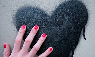 Eine Frauenhand mit rot lackierten Fingernägeln berührt in Berlin ein schwarzes Herz, das auf eine Mauer gesprüht wurde. - Verwendung weltweit Eine Frauenhand mit rot lackierten Fingernägeln berührt in Berlin ein schwarzes Herz, das auf eine Mauer gesprüht wurde. - Verwendung weltweit