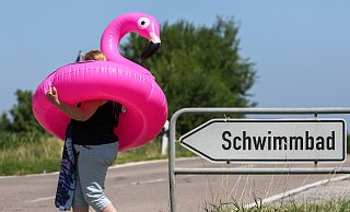 Eine Frau läuft mit einem aufblasbaren Flamingo-Schwimmring und einem Badetuch an einem Wegweiser vorbei, auf dem "Schwimmbad" geschrieben steht. - Thomas Warnack/dpa Eine Frau läuft mit einem aufblasbaren Flamingo-Schwimmring und einem Badetuch an einem Wegweiser vorbei, auf dem "Schwimmbad" geschrieben steht. - Thomas Warnack/dpa