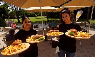 Beriwan Ahmad (l.) und Sherin Sulaiman servieren auf der Außenterrasse Pommes und Burger auf Holzbrettern. Die ersetzen den klassischen Teller. Das neue „Eiscafé und Bistro am Freibad“ hat seit vergangenem Wochenende geöffnet. - Niklas Krämer Beriwan Ahmad (l.) und Sherin Sulaiman servieren auf der Außenterrasse Pommes und Burger auf Holzbrettern. Die ersetzen den klassischen Teller. Das neue „Eiscafé und Bistro am Freibad“ hat seit vergangenem Wochenende geöffnet. - Niklas Krämer