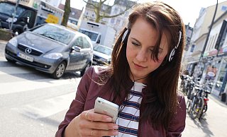 Eine junge Frau hört Musik, während sie eine Nachricht auf dem Handy schreibt. Das ist nicht verboten, aber im Straßenverkehr sehr gefährlich. - Symbolfoto: picture alliance / dpa Eine junge Frau hört Musik, während sie eine Nachricht auf dem Handy schreibt. Das ist nicht verboten, aber im Straßenverkehr sehr gefährlich. - Symbolfoto: picture alliance / dpa