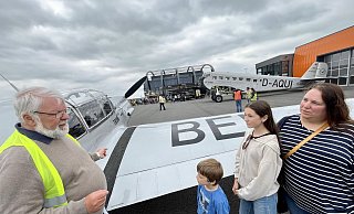 Hubert Schmidt vom Quax-Verein erzählt Levi, Lia und Katrin Seven (v. l.) Details aus der Geschichte der BF 108 aus dem Jahr 1937. Im Hintergrund sind die Ju 52 der Lufthansa und der Quax-Hangar zu sehen. - Jens Reddeker Hubert Schmidt vom Quax-Verein erzählt Levi, Lia und Katrin Seven (v. l.) Details aus der Geschichte der BF 108 aus dem Jahr 1937. Im Hintergrund sind die Ju 52 der Lufthansa und der Quax-Hangar zu sehen. - Jens Reddeker