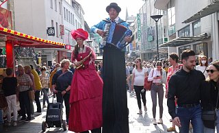 In dieser Frühlingsfest-Szenerie bahnt sich der Walcact Duo Grande auf Stelzen einen Weg durch die Westernstraße, in der Buden erkennbar sind. - Lisa Richter In dieser Frühlingsfest-Szenerie bahnt sich der Walcact Duo Grande auf Stelzen einen Weg durch die Westernstraße, in der Buden erkennbar sind. - Lisa Richter