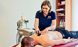 Ina Koshin (stehend) führt mit ihrem Kollegen Sergej Röhrig (liegend) die Anwendung der WINBACK Therapie vor. Der Körper wird über das Gerät bei der Behandlung stimuliert, der Patient fühlt eine leichte und entspannende Wärme. - Wencke Meckenstock Ina Koshin (stehend) führt mit ihrem Kollegen Sergej Röhrig (liegend) die Anwendung der WINBACK Therapie vor. Der Körper wird über das Gerät bei der Behandlung stimuliert, der Patient fühlt eine leichte und entspannende Wärme. - Wencke Meckenstock