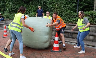 Mit vereinten Kräften rollen die Mitglieder der Gruppe Pegelclub & Friends den rund 350 Kilogramm schweren Strohballen durch den Hindernis-Parcours auf dem Pemberville Platz. - Shannon-Lee Bendig Mit vereinten Kräften rollen die Mitglieder der Gruppe Pegelclub & Friends den rund 350 Kilogramm schweren Strohballen durch den Hindernis-Parcours auf dem Pemberville Platz. - Shannon-Lee Bendig