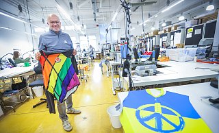 Textilproduktion in Bielefeld: Ralf Kelber steht mit einer bunt bedruckten Jacke in der Näherei seines Unternehmens. Vorn rechts liegt ein Laufshirt, das in kürzester Zeit für die Hermannsläufer eines Bielefelder Unternehmens entwickelt wurde. In den Farben der Ukraine zeigt es ein Peace-Symbol und die Sparrenburg. - Sarah Jonek Fotografie Textilproduktion in Bielefeld: Ralf Kelber steht mit einer bunt bedruckten Jacke in der Näherei seines Unternehmens. Vorn rechts liegt ein Laufshirt, das in kürzester Zeit für die Hermannsläufer eines Bielefelder Unternehmens entwickelt wurde. In den Farben der Ukraine zeigt es ein Peace-Symbol und die Sparrenburg. - Sarah Jonek Fotografie