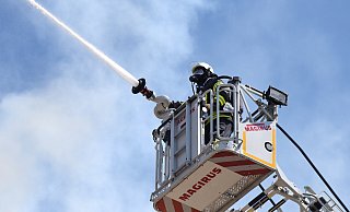 Ein Feuerwehrmann in voller Ausrüstung steht im Korb der Drehleiter, von wo er die Flammen auf dem Dach des Golden Tulip Hotel bekämpft. Die enorme Hitze von vorne, aber auch von oben und in der Kleidung lassen den Schweiß nur so fließen. - Barbara Franke Ein Feuerwehrmann in voller Ausrüstung steht im Korb der Drehleiter, von wo er die Flammen auf dem Dach des Golden Tulip Hotel bekämpft. Die enorme Hitze von vorne, aber auch von oben und in der Kleidung lassen den Schweiß nur so fließen. - Barbara Franke