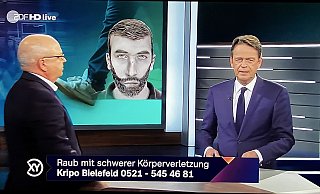 Kriminalhauptkommissar Thomas Grothaus gibt Rudi Cerne live im TV Auskunft zu dem Raubüberfall. Hinten ist das Phantomfoto des Täter s zu sehen. - Screenshot: ZDF / Aktenzeichen XY Kriminalhauptkommissar Thomas Grothaus gibt Rudi Cerne live im TV Auskunft zu dem Raubüberfall. Hinten ist das Phantomfoto des Täter s zu sehen. - Screenshot: ZDF / Aktenzeichen XY