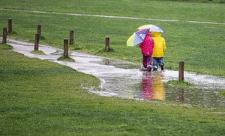 Zwei Kinder laufen in einem Park durch eine große Pfütze. - Fabian Sommer Zwei Kinder laufen in einem Park durch eine große Pfütze. - Fabian Sommer