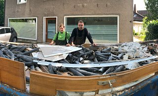 Nathalie Witt und Max König stehen vor einer von vier großen Mulden mit Abfall aus dem vollgelaufenen Keller ihres Hauses (im Hintergrund). - Thomas Reineke Nathalie Witt und Max König stehen vor einer von vier großen Mulden mit Abfall aus dem vollgelaufenen Keller ihres Hauses (im Hintergrund). - Thomas Reineke