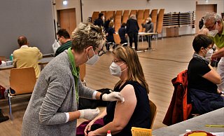 Hildegard Stallein gibt die Corona-Impfung in den Arm einer Patientin. Im Hintergrund warten bereits die nächsten Impfwilligen an der Anmeldung. - Raphael Athens Hildegard Stallein gibt die Corona-Impfung in den Arm einer Patientin. Im Hintergrund warten bereits die nächsten Impfwilligen an der Anmeldung. - Raphael Athens