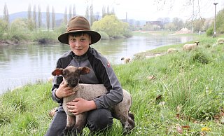 Nachwuchs-Schäfer Lennard Schrick mit einem etwa drei Wochen alten Lämmchen der Wanderschäferei Schrick. Gemeinsam mit der „Kinderstube“, einer Gruppe von 80 Schafen mit jeweils Zwillingen, weidet das Lämmchen nun am Weserufer auf dem Gelände der Landesgartenschau. - LGS Höxter/Madita Schellenberg Nachwuchs-Schäfer Lennard Schrick mit einem etwa drei Wochen alten Lämmchen der Wanderschäferei Schrick. Gemeinsam mit der „Kinderstube“, einer Gruppe von 80 Schafen mit jeweils Zwillingen, weidet das Lämmchen nun am Weserufer auf dem Gelände der Landesgartenschau. - LGS Höxter/Madita Schellenberg