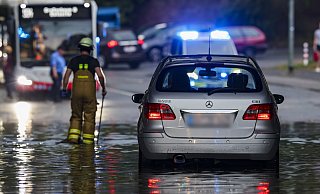 Duisburg: Ein Auto steckt im Hochwasser in einer Senke fest, während Feuerwehrleute die Gullydeckel öffnen, damit das Wasser ablaufen kann. - Christoph Reichwein Duisburg: Ein Auto steckt im Hochwasser in einer Senke fest, während Feuerwehrleute die Gullydeckel öffnen, damit das Wasser ablaufen kann. - Christoph Reichwein