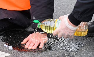 Polizisten lösen die festgeklebten Hände der Klima-Aktivisten mit Speiseöl von der Straße. - Julian Stratenschulte / dpa Polizisten lösen die festgeklebten Hände der Klima-Aktivisten mit Speiseöl von der Straße. - Julian Stratenschulte / dpa