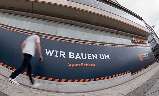 "Wir bauen um" steht auf dem Sportscheck-Gebäude am Jahnplatz - und das noch sehr lange. - Oliver Krato "Wir bauen um" steht auf dem Sportscheck-Gebäude am Jahnplatz - und das noch sehr lange. - Oliver Krato