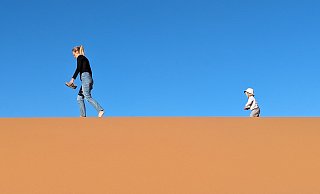 Angekommen im größten Sandkasten der Welt, der Sahara: Mutter und Kind spazieren vor leuchtend blauem Himmel durch die Dünen. - privat Angekommen im größten Sandkasten der Welt, der Sahara: Mutter und Kind spazieren vor leuchtend blauem Himmel durch die Dünen. - privat