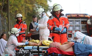 Rettungskräfte sind mit weißen Schutzanzügen bekleidet, um die Verletzten aus möglicherweise kontaminiertem Qualm zu holen. Reibungslos läuft das Zusammenspiel zwischen Rettungsdienst und Einsatzkräften der Feuerwehr. - Charlotte Mahncke Rettungskräfte sind mit weißen Schutzanzügen bekleidet, um die Verletzten aus möglicherweise kontaminiertem Qualm zu holen. Reibungslos läuft das Zusammenspiel zwischen Rettungsdienst und Einsatzkräften der Feuerwehr. - Charlotte Mahncke