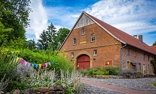 Der Namensstein auf der Pflanzeninsel vor dem Haupthaus von Hof Ramsbrock ist von Wildblumen fast überwucher, das springende Schaf kaum noch erkennbar. - Mike-Dennis Mueller / www.mdm.photo Der Namensstein auf der Pflanzeninsel vor dem Haupthaus von Hof Ramsbrock ist von Wildblumen fast überwucher, das springende Schaf kaum noch erkennbar. - Mike-Dennis Mueller / www.mdm.photo