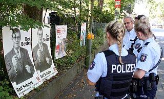 Dietmar Krämer von der BfB erklärt den Polizeibeamten, dass sie vor einem alten Wahlplakat ihres 2014 verstorbenen Parteikollegen Ralf Schulze stehen. - Jens Reichenbach Dietmar Krämer von der BfB erklärt den Polizeibeamten, dass sie vor einem alten Wahlplakat ihres 2014 verstorbenen Parteikollegen Ralf Schulze stehen. - Jens Reichenbach