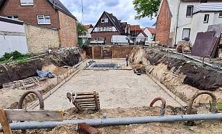 Die teilweise mit weißem Sand verdeckten dunklen Bögen links und rechts der Baugrube dokumentieren das Profil des doppelten Stadtgrabens. - Birgit Vredenburg Die teilweise mit weißem Sand verdeckten dunklen Bögen links und rechts der Baugrube dokumentieren das Profil des doppelten Stadtgrabens. - Birgit Vredenburg