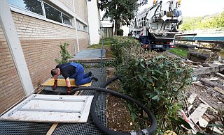 Ein Mitarbeiter des Spezialentsorgers hält an einer Schule den Schlauch in den Keller. - picture alliance/dpa Ein Mitarbeiter des Spezialentsorgers hält an einer Schule den Schlauch in den Keller. - picture alliance/dpa