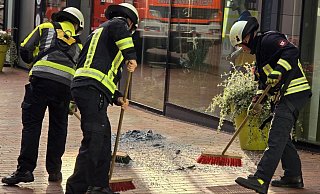 Die Einsatzkräfte der Gütersloher Berufsfeuerwehr kehren die Glassplitter der herabgestürzten Fassadenscheibe zusammen. - Kevin Hermann Die Einsatzkräfte der Gütersloher Berufsfeuerwehr kehren die Glassplitter der herabgestürzten Fassadenscheibe zusammen. - Kevin Hermann