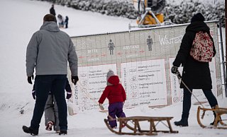Ausflüger mit Schlitten gehen in Winterberg an einer geschlossenen Skipiste an einem Banner mit Corona-Verhaltensregeln vorbei. - picture alliance/dpa Ausflüger mit Schlitten gehen in Winterberg an einer geschlossenen Skipiste an einem Banner mit Corona-Verhaltensregeln vorbei. - picture alliance/dpa