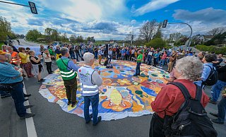 Die Demonstranten haben mitten auf der Herforder Straße ein großes buntes Tuch ausgebreitet und halten eine kurze Kundgebung ab. - Andreas Zobe Die Demonstranten haben mitten auf der Herforder Straße ein großes buntes Tuch ausgebreitet und halten eine kurze Kundgebung ab. - Andreas Zobe