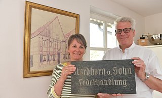 Andrea und Wilhelm Nordhorn halten das Firmenschild der 1910 von Wilhelms Großvater Franz gegründeten Lederhandlung. 1950 wurde der an der Königstraße ansässige Sitz (Bild im Hintergrund) der früheren Schäftemacherei nach Niehorst transloziert. Foto: Jens Dünhölter Andrea und Wilhelm Nordhorn halten das Firmenschild der 1910 von Wilhelms Großvater Franz gegründeten Lederhandlung. 1950 wurde der an der Königstraße ansässige Sitz (Bild im Hintergrund) der früheren Schäftemacherei nach Niehorst transloziert. Foto: Jens Dünhölter