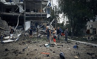 Ukraine: Menschen stehen, von Trümmern umgeben, vor zerstörten Gebäuden. - Kostiantyn Liberov/AP/dpa Ukraine: Menschen stehen, von Trümmern umgeben, vor zerstörten Gebäuden. - Kostiantyn Liberov/AP/dpa
