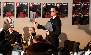 Pressekonferenz in der Stern-Redaktion: Gerd Heidemann (Lars Eidinger) präsentiert die Hitler Tagebücher und liest aus ihnen vor. - RTL / Martin Valentin Menke Pressekonferenz in der Stern-Redaktion: Gerd Heidemann (Lars Eidinger) präsentiert die Hitler Tagebücher und liest aus ihnen vor. - RTL / Martin Valentin Menke